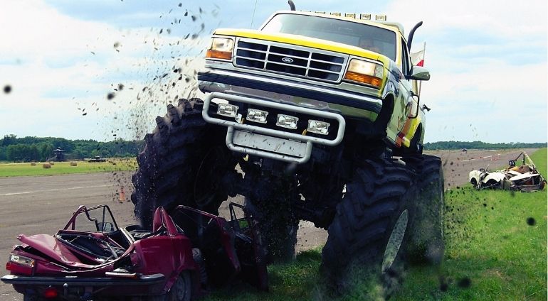 Biały Monster Truck Wjeżdża Na Samochód i Rozrzuca Błoto